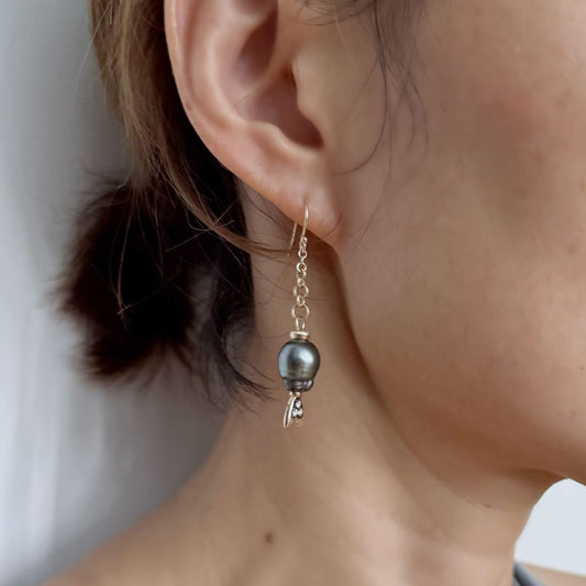 Close-up of an earring with a black Tahitian pearl drop worn on a model.
